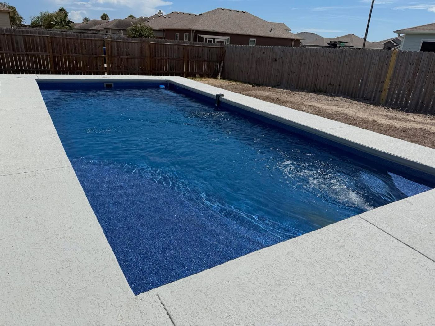A real Kinetic rectangular fiberglass pool with a full concrete surround in a fenced backyard