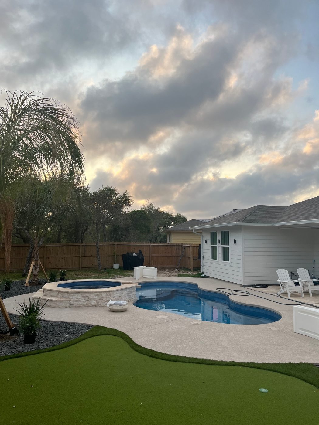 A real Kinetic freeform fiberglass pool with a spa and turf lawn photographed at dusk