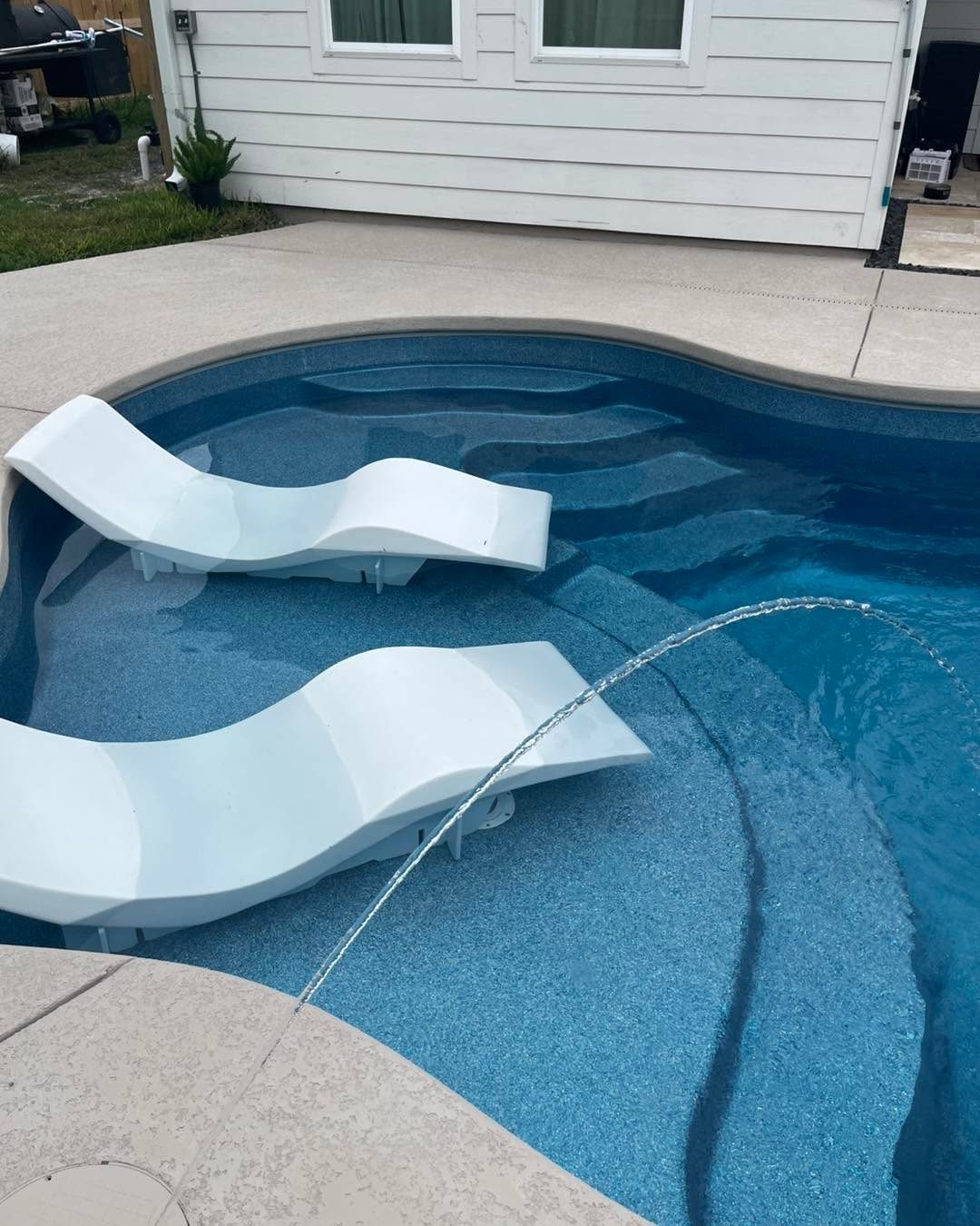 A real Kinetic freeform fiberglass pool with laminar deck jets arcing over a sun shelf