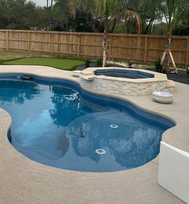 A real Kinetic freeform fiberglass pool with a raised spa and a turf lawn