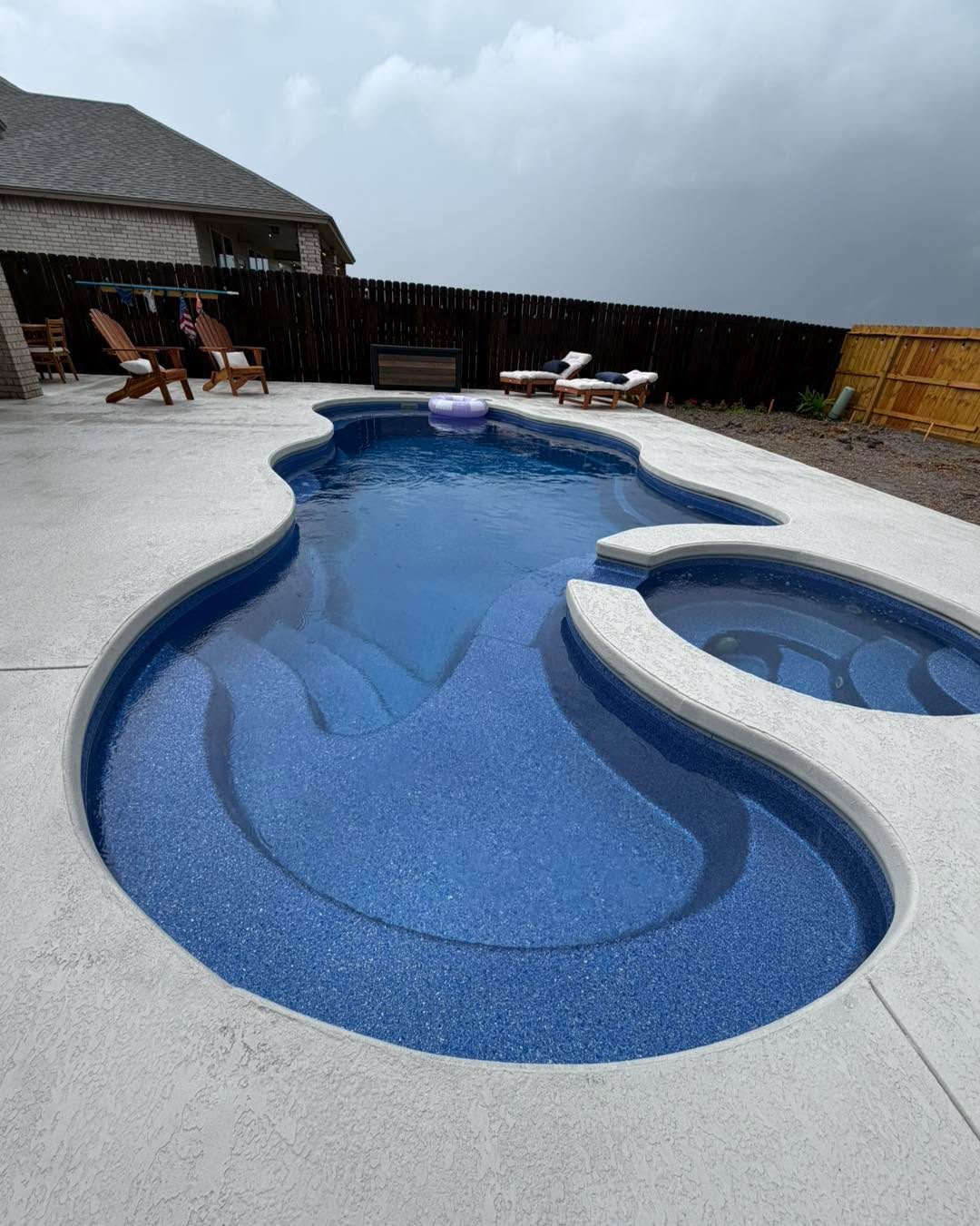 A real Kinetic freeform fiberglass pool with built-in bench seating and a broom-finish concrete deck